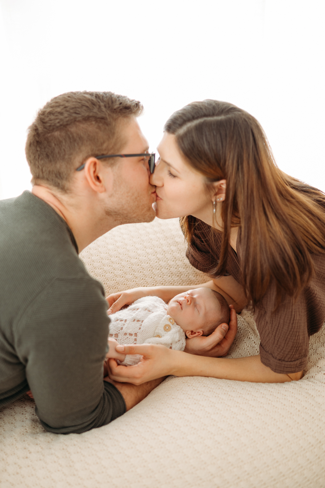 Mama küsst Papa in den Händen hält der frischgebackene Papa sein kleines Baby